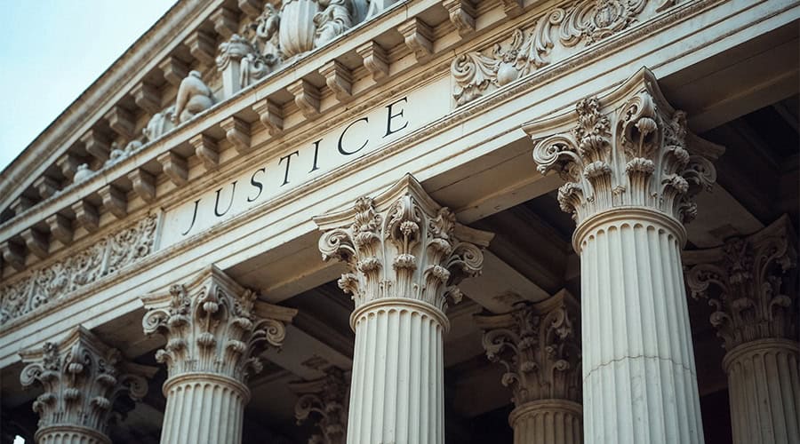 Looking up at a judicial building. Above ornate columns is the word Justice.